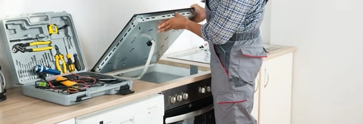 Cooktop repair technician lifting a built-in stovetop for service in Dayton, OH