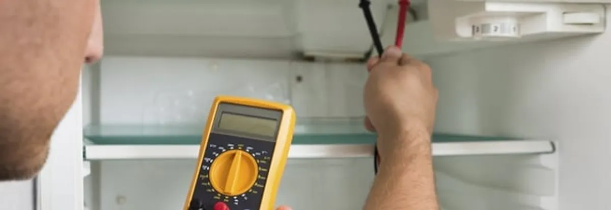 Refrigerator repair technician testing electrical components with a multimeter in Dayton, OH