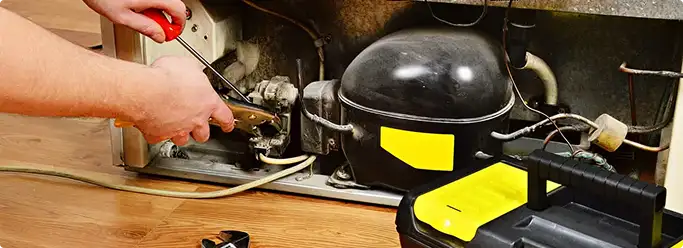 Refrigerator repair technician fixing the compressor and wiring in Dayton, OH
